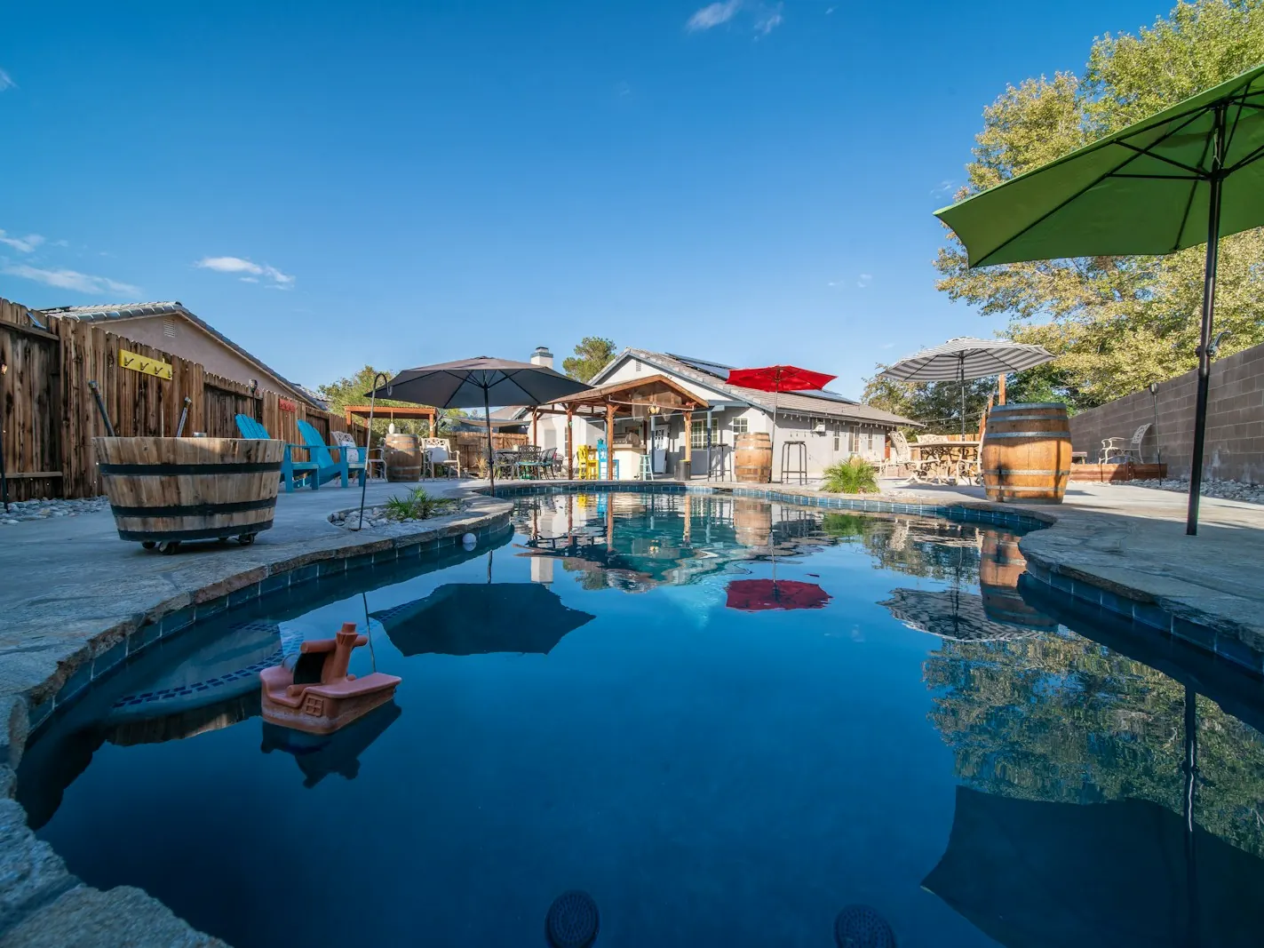 Backyard swimming pool with calm blue water, a patio and a green umbrella on a sunny day