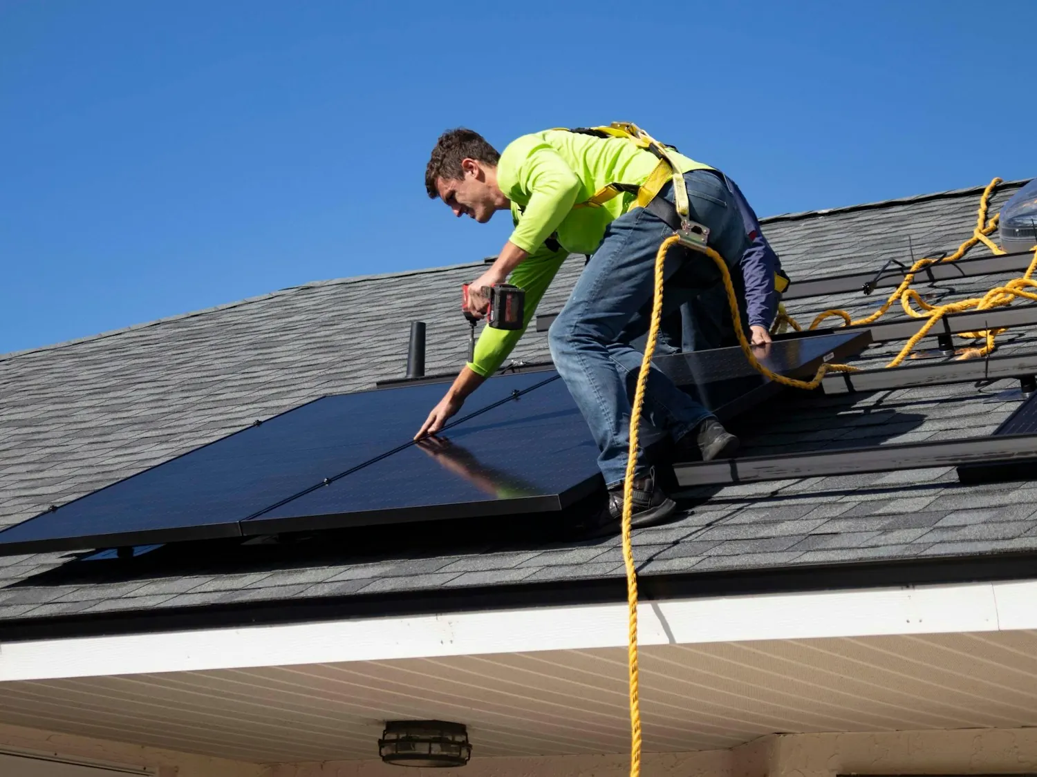 Brightreef installer fitting a black solar panel on a shingle roof under a clear blue sky
