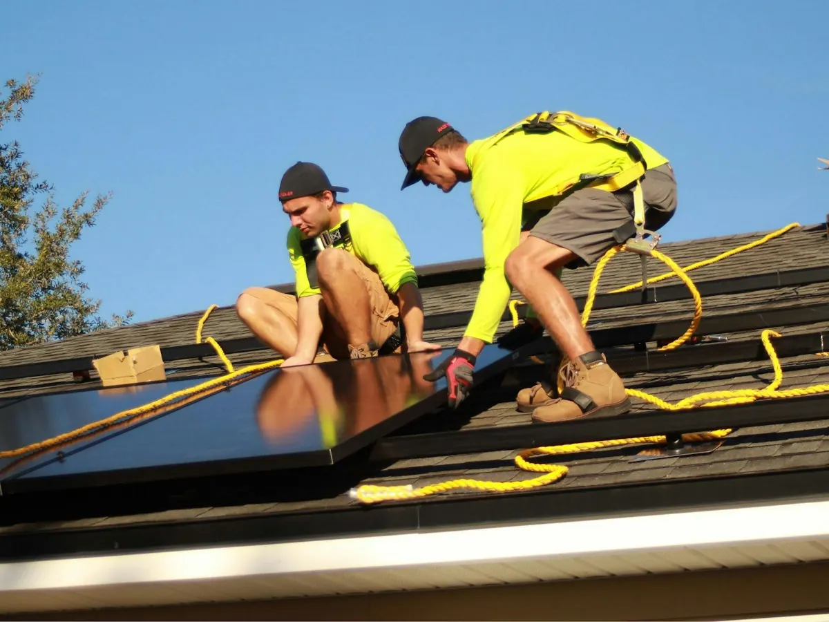 Two Brightreef installers in high-visibility shirts securing a solar panel on a roof