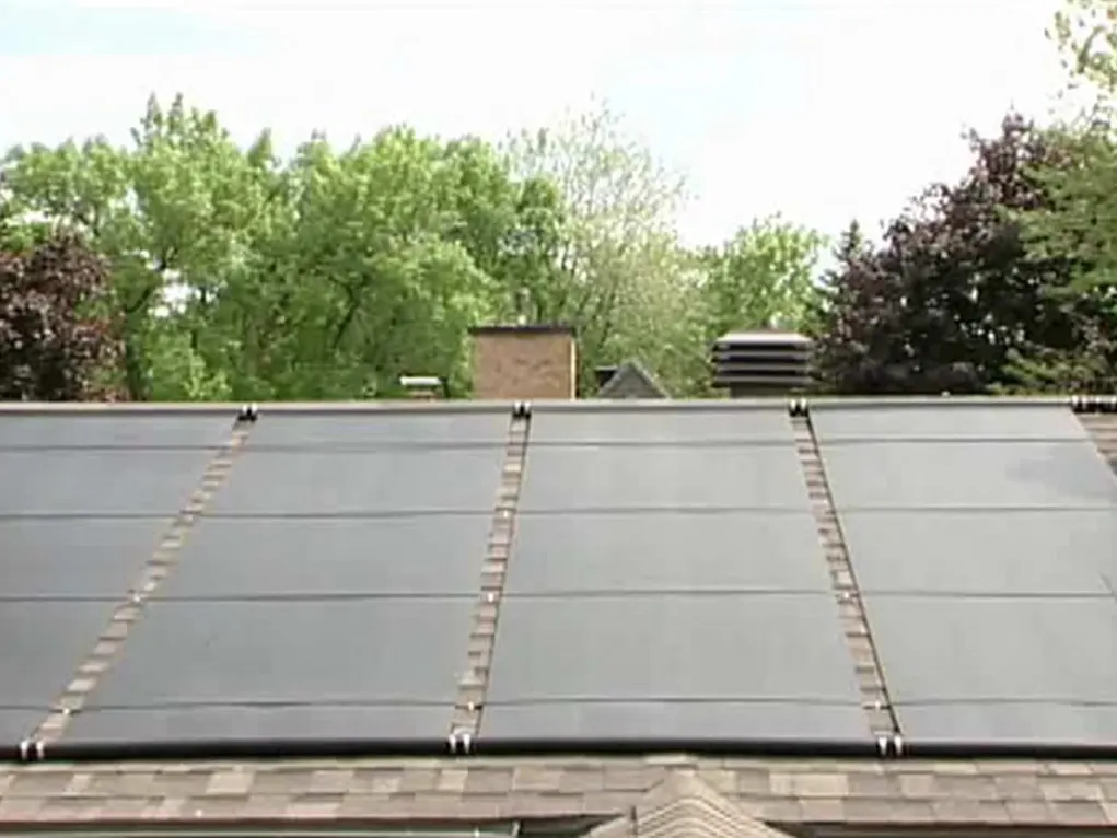 Solar pool-heating panels covering a shingle roof in a leafy neighbourhood