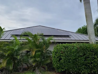 Metal-roof house with solar panels behind a tall green hedge