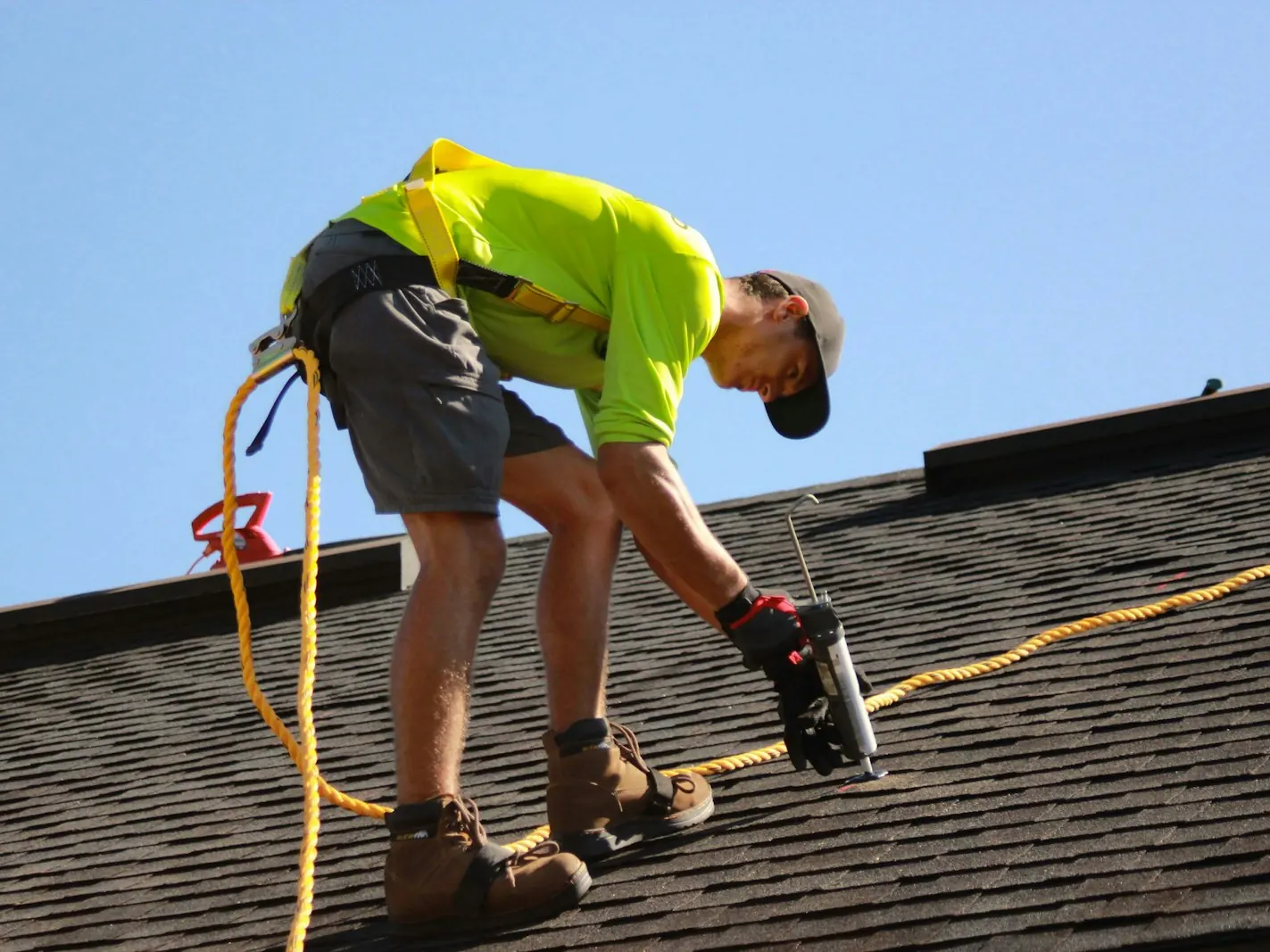 Roofer in a safety harness fixing shingles on a pitched roof