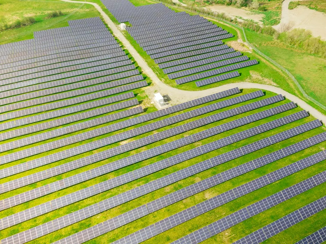 Aerial view of long rows of solar panels on green farmland