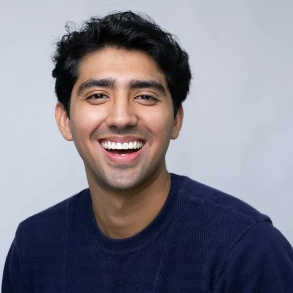 Portrait of Arjun Mehta smiling in a navy sweater against a grey background