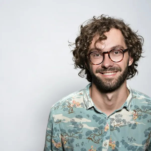 Portrait of Lucas Brenner with curly hair and glasses wearing a patterned shirt